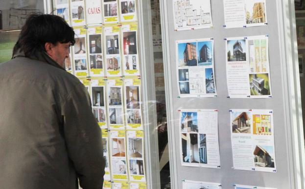 Un hombre observa anuncios de venta de pisos en el escaparate de una inmobiliaria.