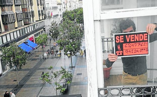 Una persona coloca un cartel de 'se vende' en la ventana de un piso. 