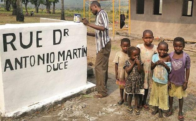 Un hombre, acompañado por un grupo de niñas, pinta el muro con el nombre de una de las calles que llega al futuro primer hospital materno-infantil de la R.D. del Congo.