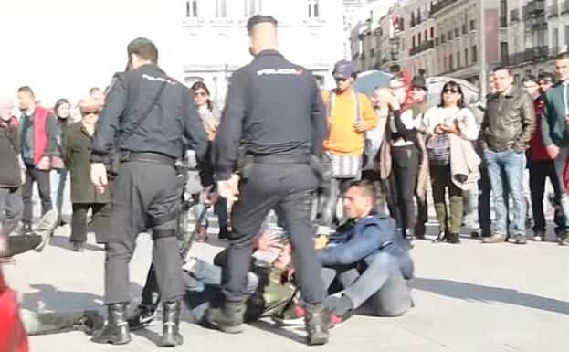 El policía propina una patada a uno de los mendigos.