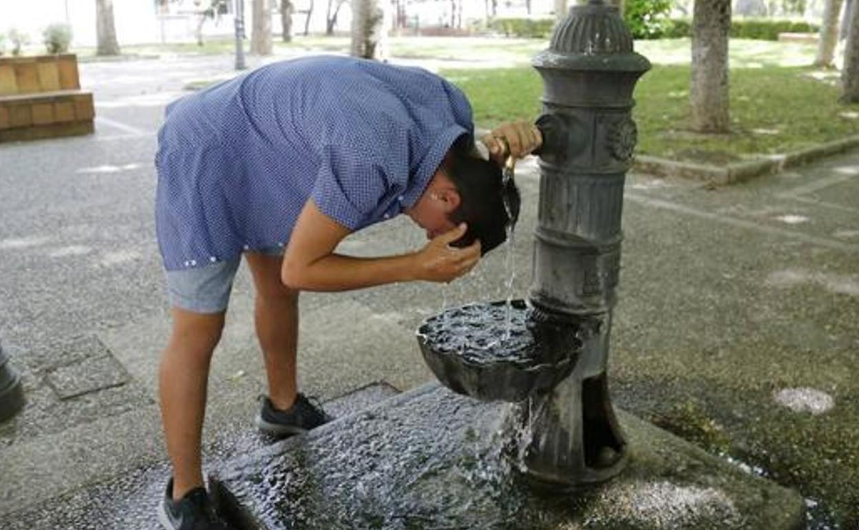 Un joven se refresca en una fuente. 