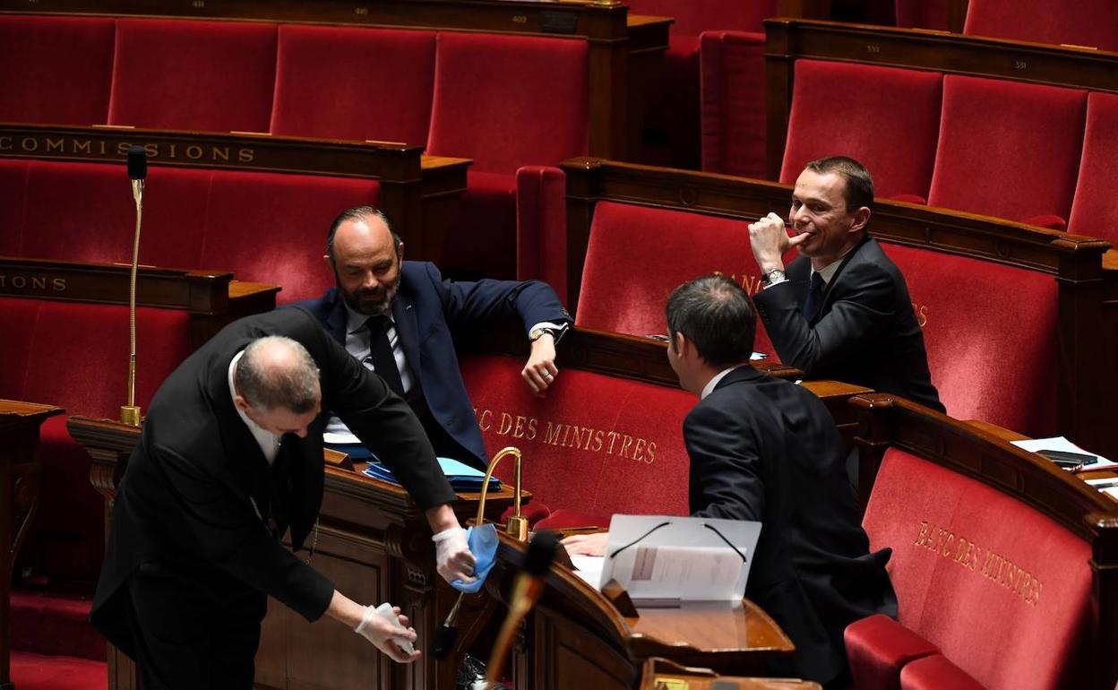 Varios ministros hablan entre ellos, mientras un trabajador de la Asamblea Nacional de Francia desinfecta el micrófono.