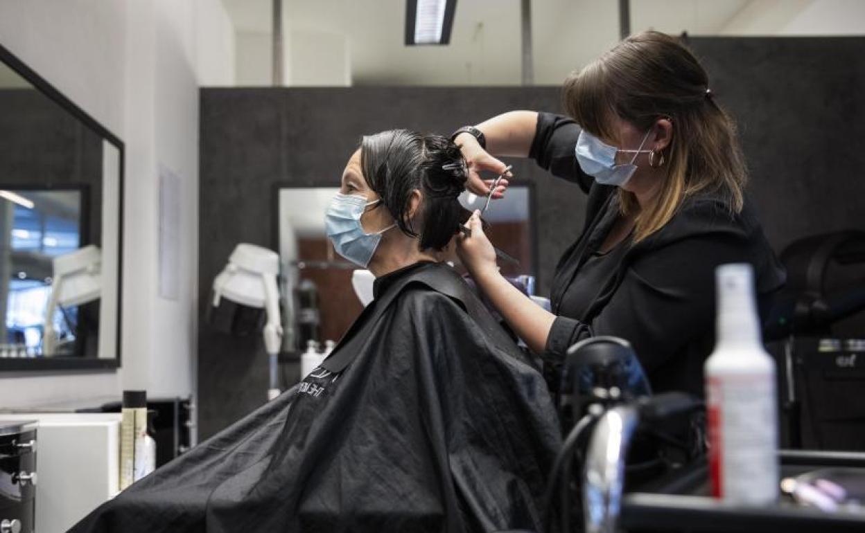 Una peluquera corta el pelo a una mujer con una máscara facial protectora contra el coronavirus en una peluquería de Berna, Suiza.