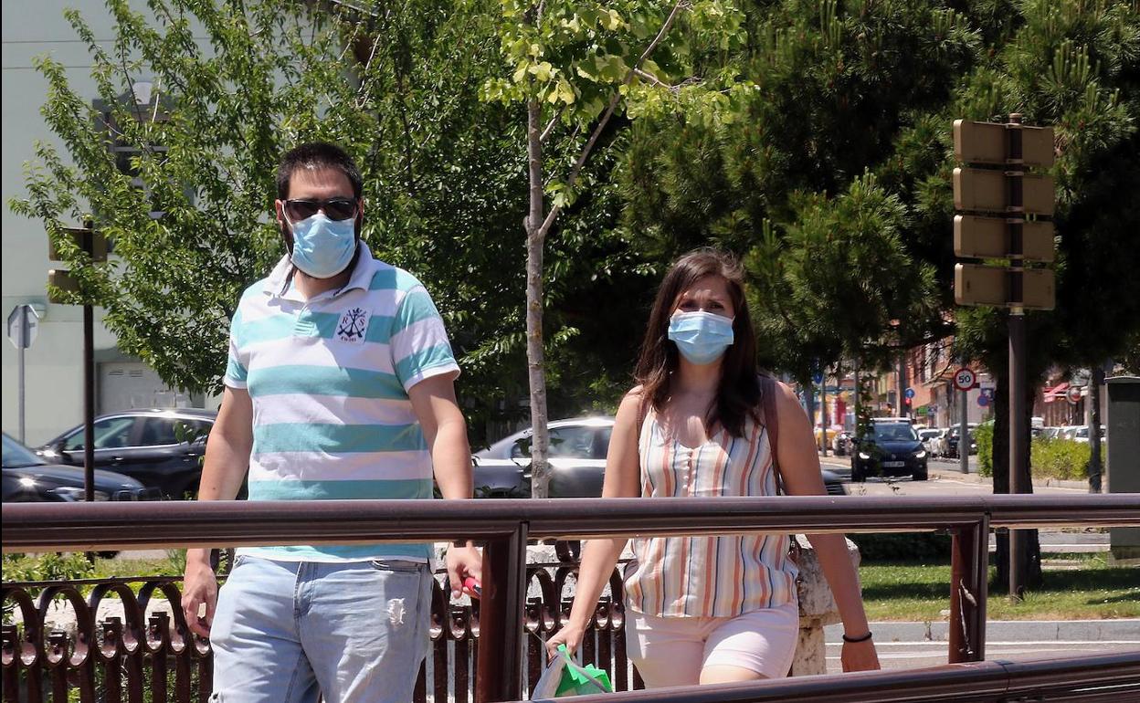 Dos personas caminan por el Puente Mayor ataviadas con sendas mascarillas.