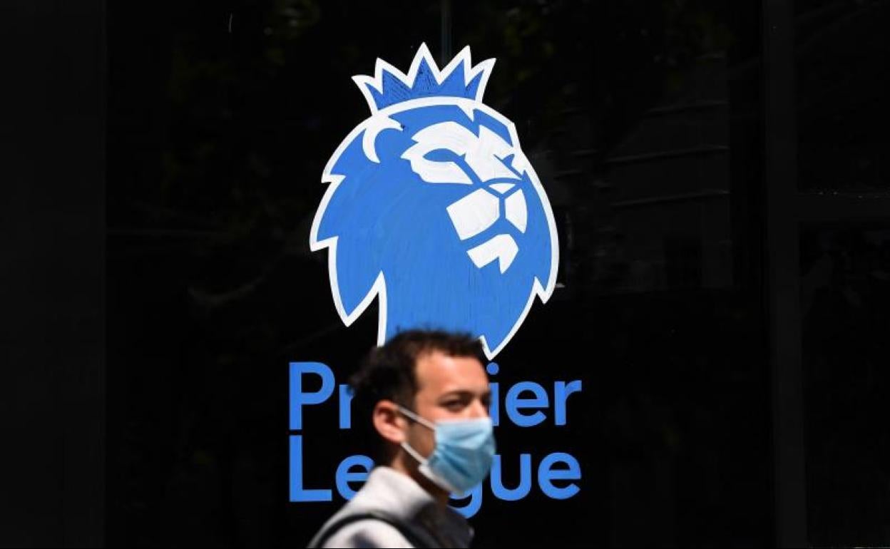 Un hombre con mascarilla pasa junto al logotipo de la Premier League. 