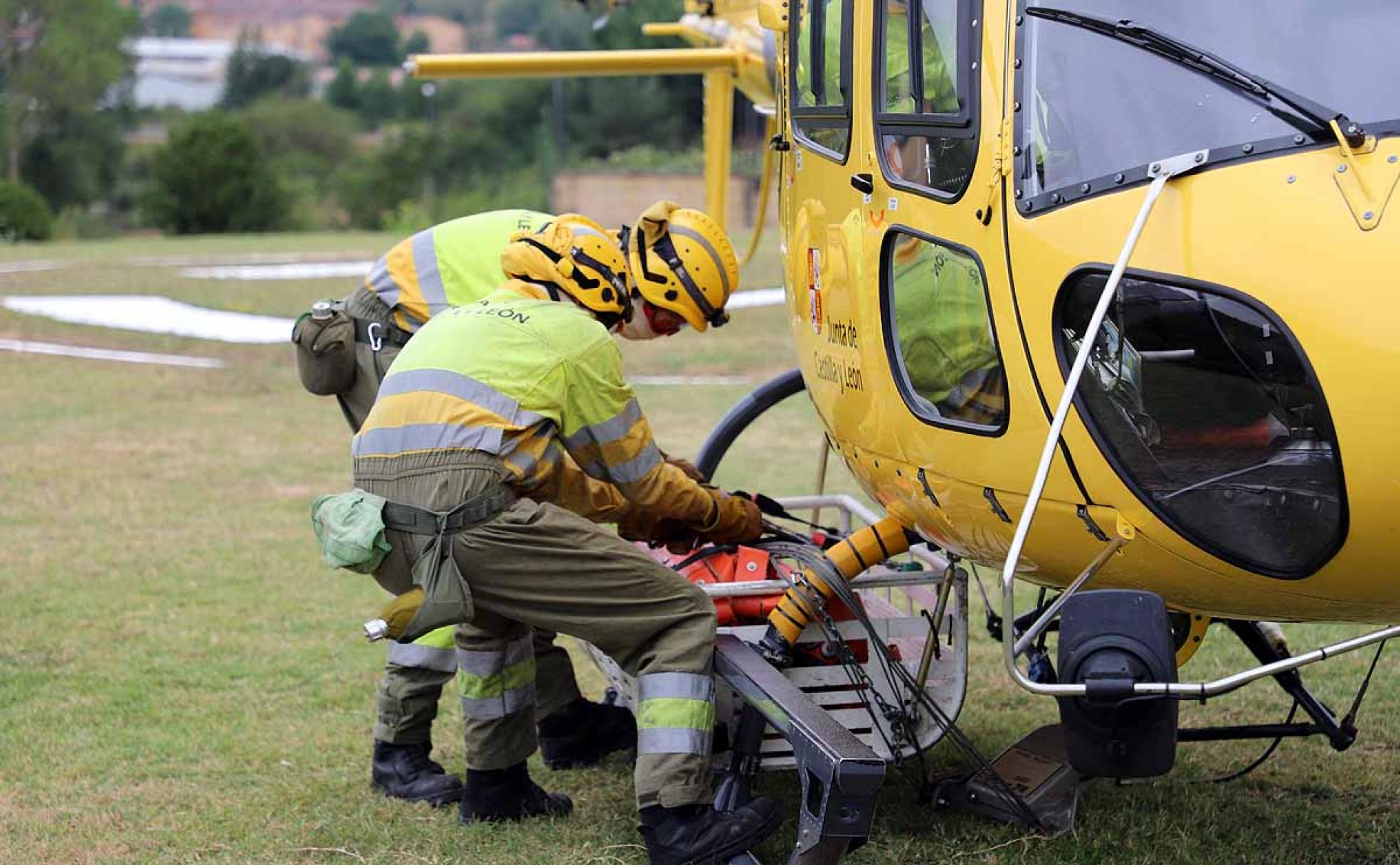 Dos trabajadores de la brigada encargada del helicóptero contra incendios de Pradoluengo instalan la bolsa con la que se recoge el agua. 