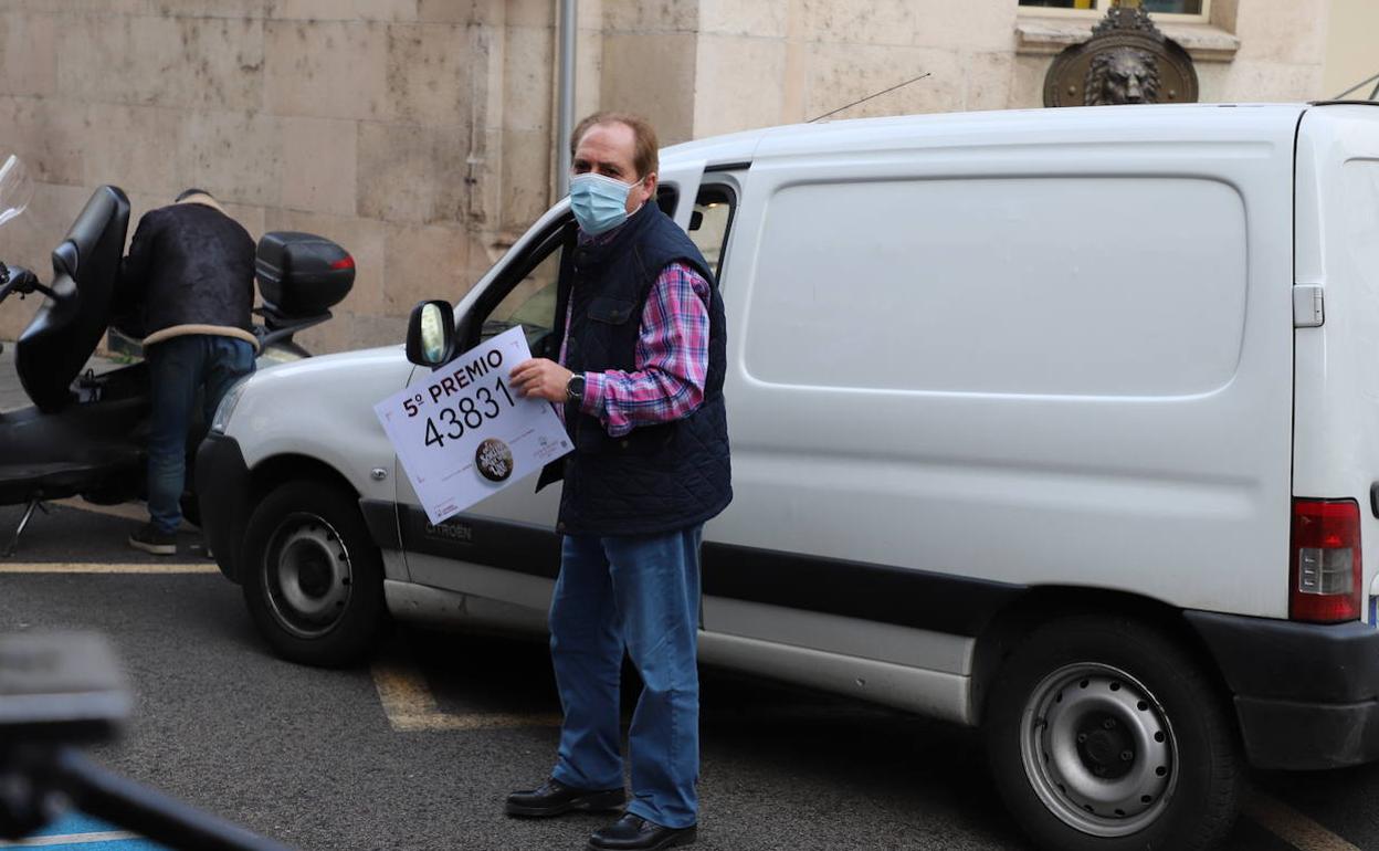 Un empleado de la delegación de Loterías y Apuestas del Estado en Burgos llega a la administración que vendió el décimo con el cartel anunciador.