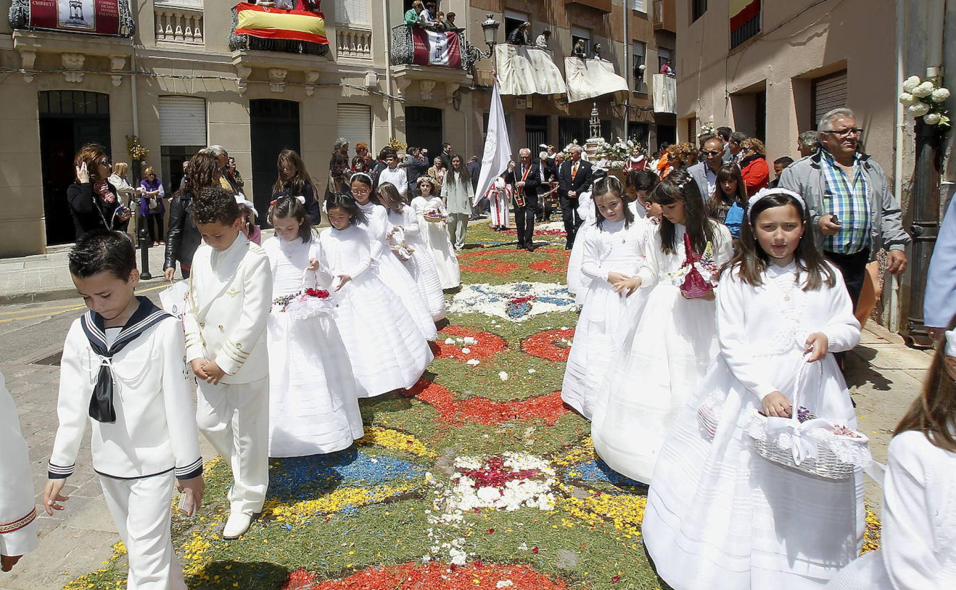 Niños y niñas de Primera Comunión preceden al Santísimo sobre las alfombras de flores durante la procesión del Corpus Christi en Carrión.