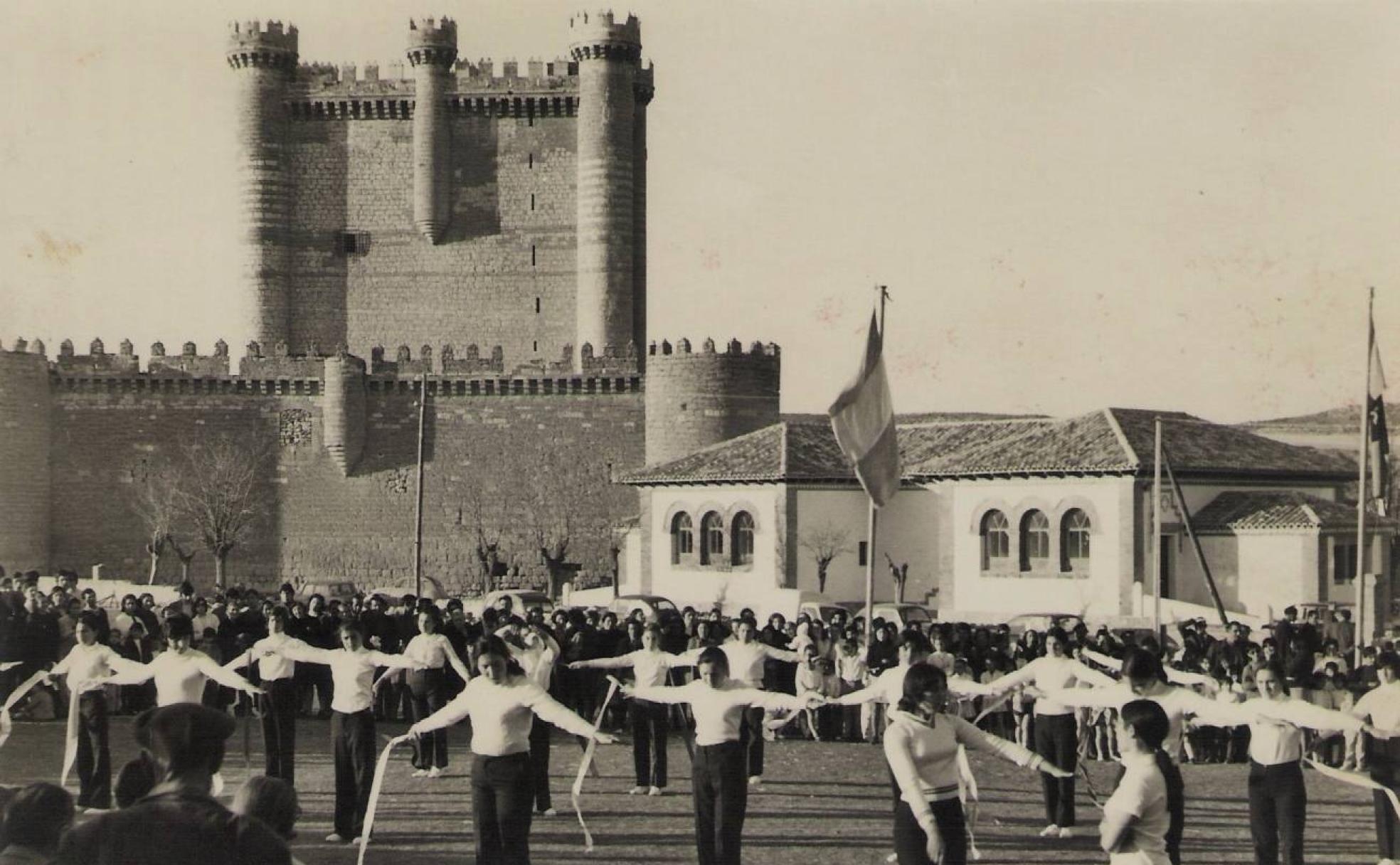 Imagen antigua de Fuensaldaña, con el castillo al fondo y un grupo de jóvenes practicando el juego de las cintas.