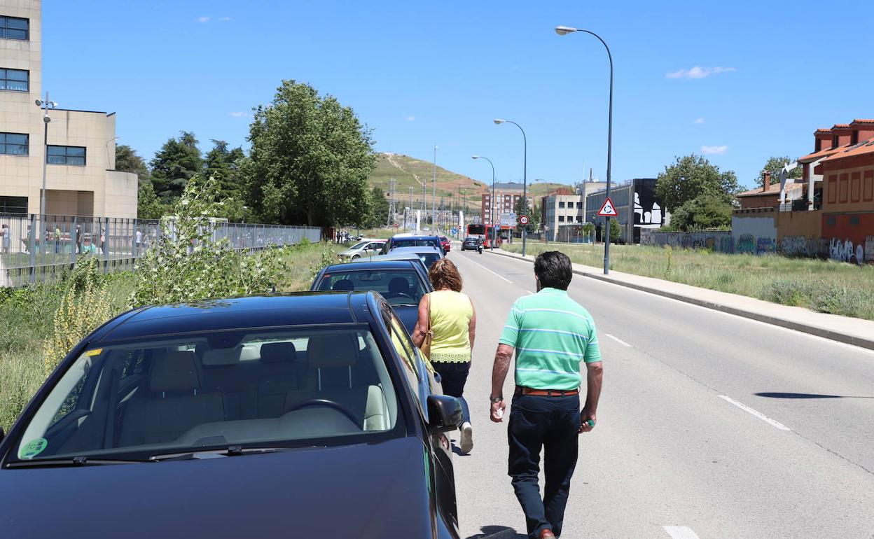 Dos personas caminan por la calzada de la calle Puente la Reina entre una hilera de coches.