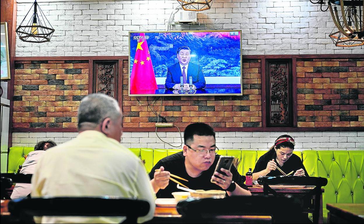 Varios clientes de un restaurante de Pekín comen ajenos al discurso televisado de Xi Jinping para presentar el plan de limpieza fiscal. 
