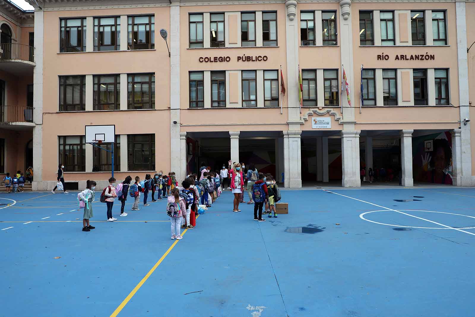 Una profesora saluda con el cole a uno de sus alumnos.