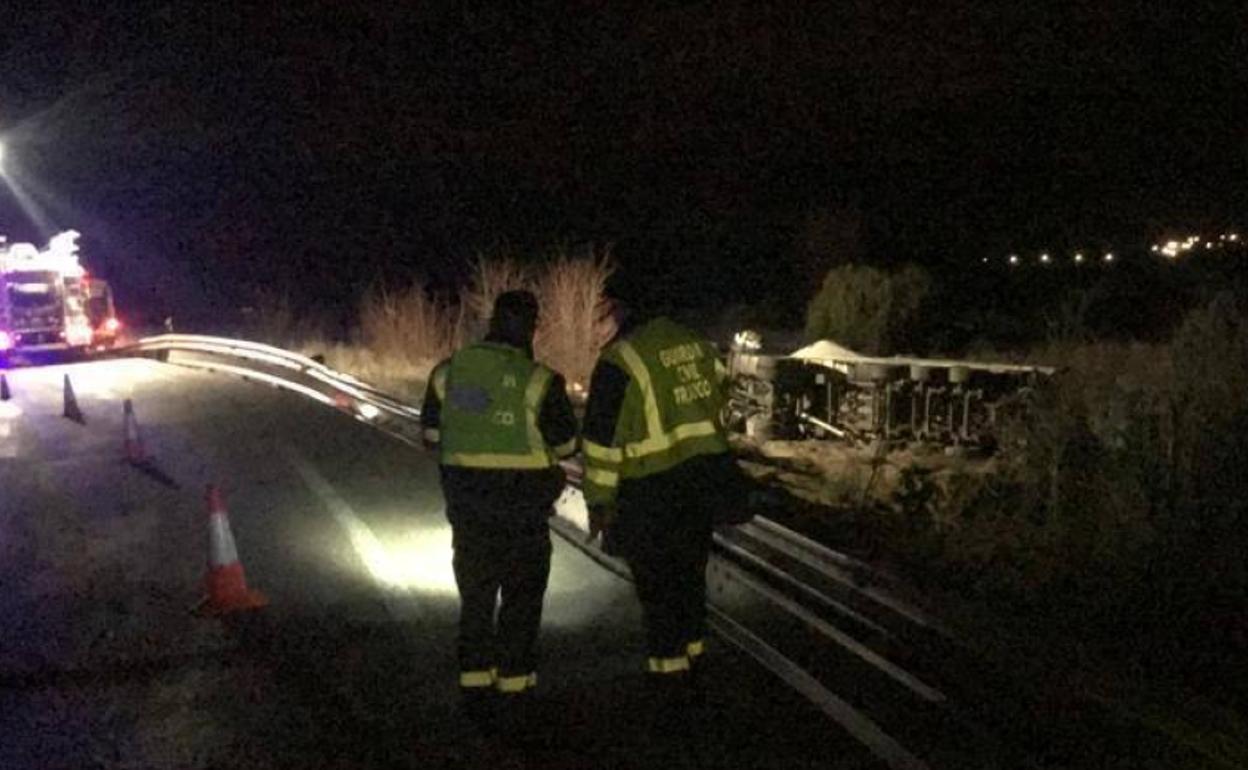 Los servicios de emergencia trabajan en el lugar del suceso, con el camión accidentado al fondo.