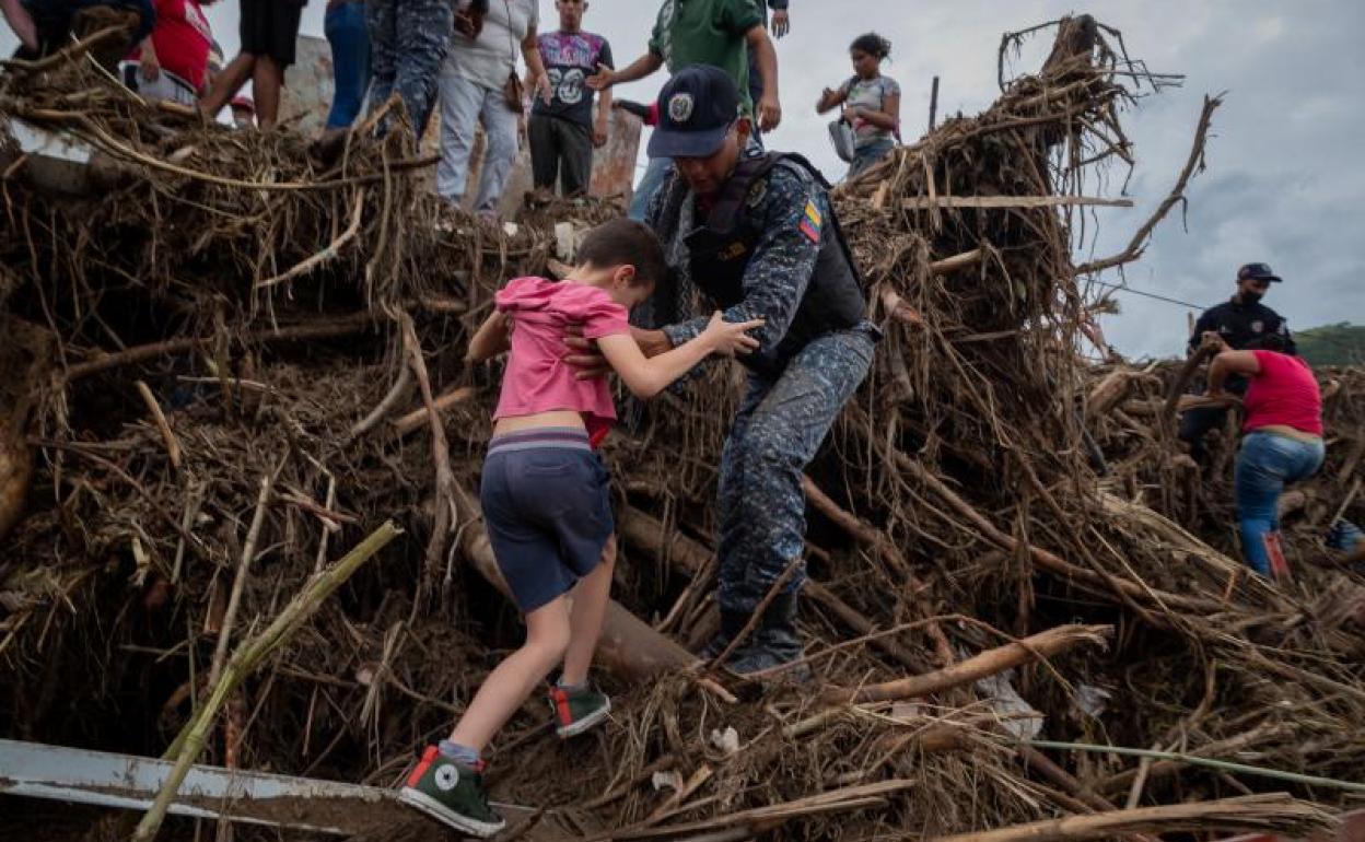 Un policía ayuda a cruzar a un niño en una zona de destrozos en Las Tejerías. 