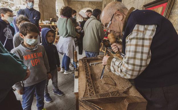 Un artesano labra una pieza de madera, ante la atenta mirada de los niños. 