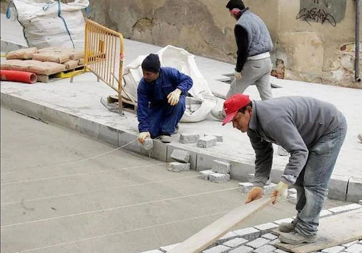 Un grupo de operarios migrantes trabaja en labores en una calzada.