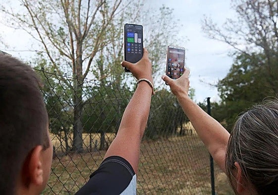 Dos personas buscan cobertura con sus teléfonos móviles en un pueblo.