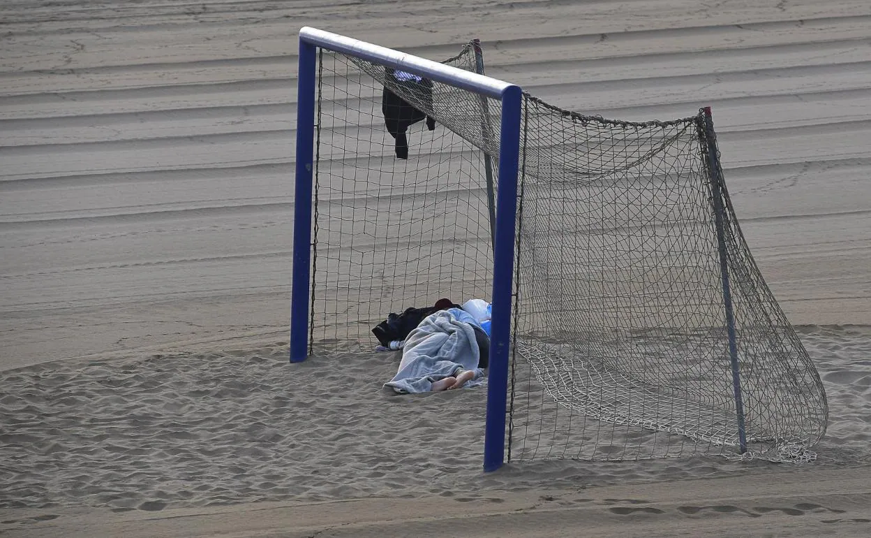 Una persona dormía en la mañana de este viernes bajo una portería de la playa de Las Alcaravaneras. 