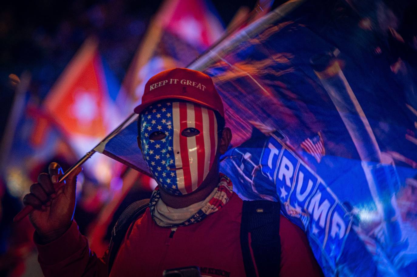 Un simpatizante de Donald Trump viste careta con la bandera estadounidense y una gorra que dice "Mantén (América) grandiosa" en el icónico café Versailles de la Calle Ocho en Miami, Florida.