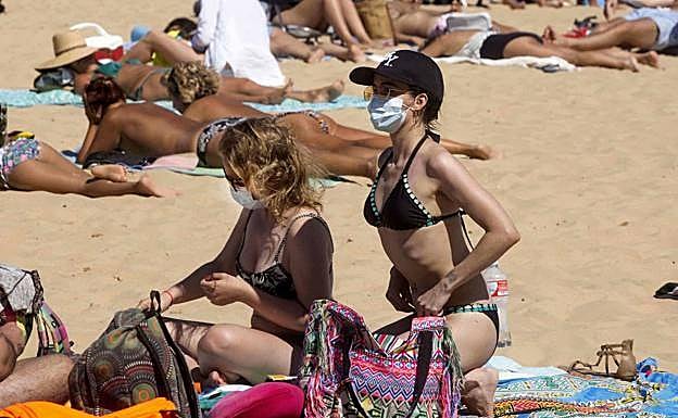Imagen de una usuaria en una playa con mascarilla mientras toma el sol. 