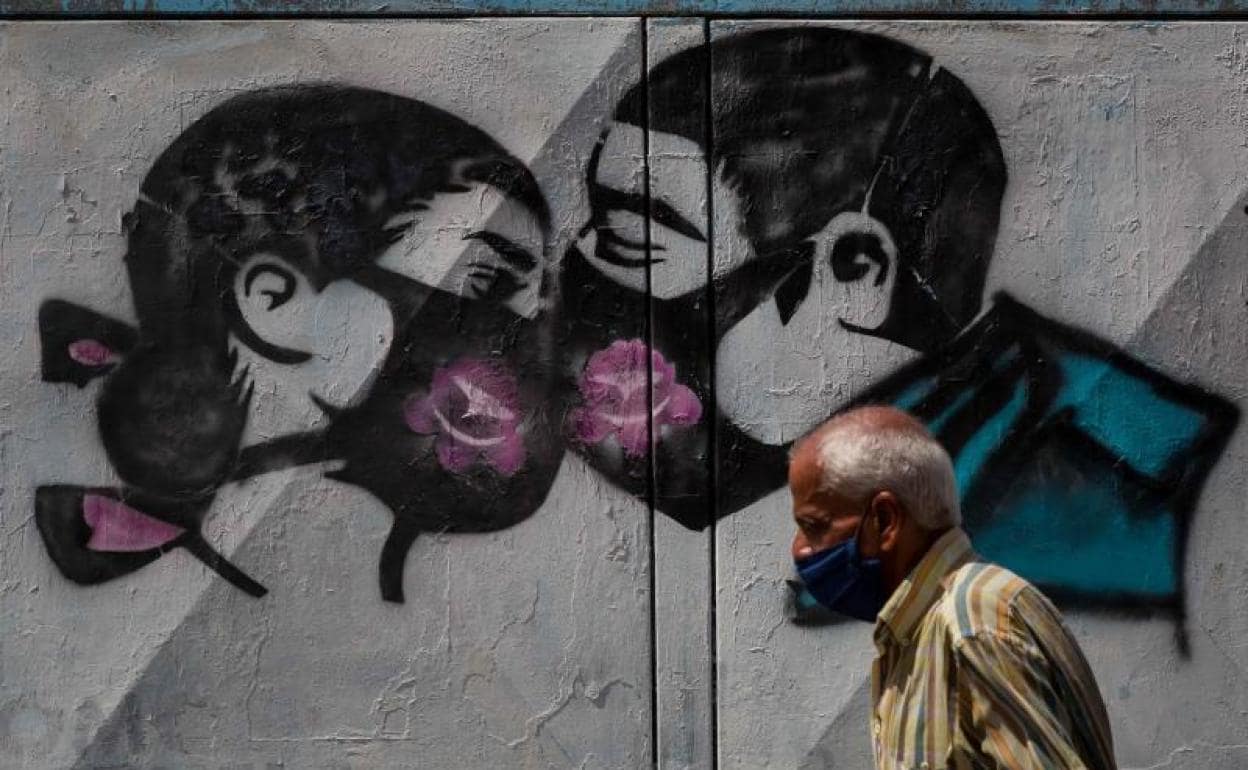 Un mural de dos jóvenes besándose con mascarilla. 