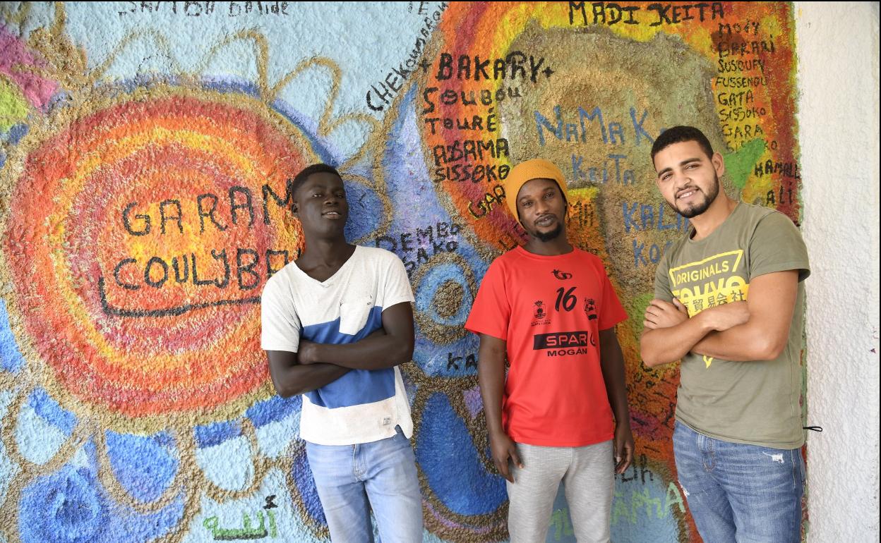Tres de los chicos alojados en el Puerto Calma posan delante de un mural que pintaron entre todos. Subsaharianos y magrebíes conviven en armonía, como si fueran una familia. 