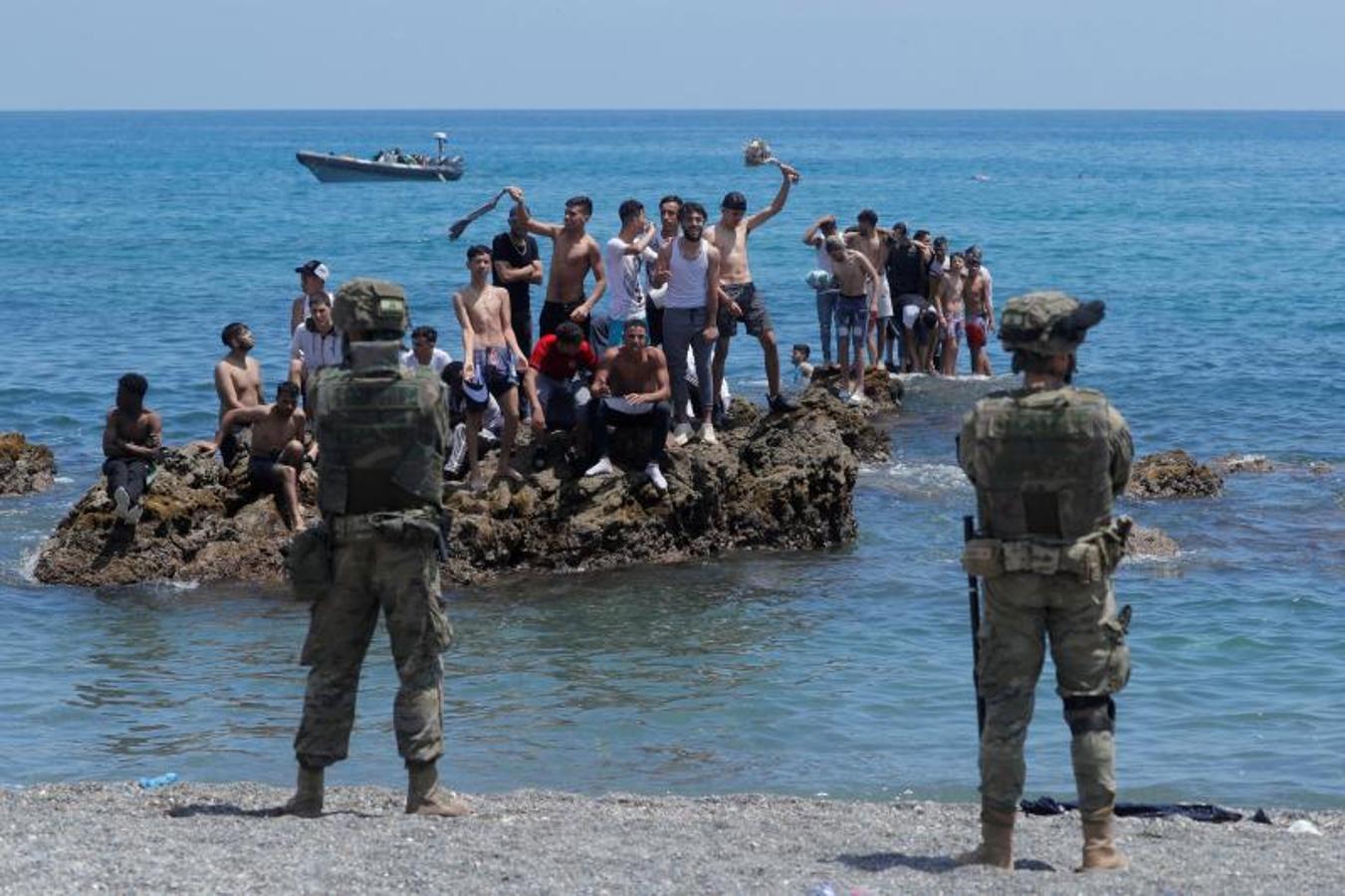 Ciudadanos marroquíes parados en las rocas frente a legionarios españoles en la playa de El Tarajal.