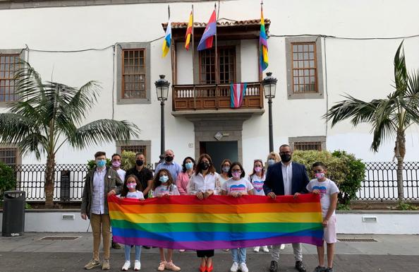 Representantes de varios colectivos LGTBI+ posan junto a las autoridades municipales con la bandera del Orgullo delante de las Casas Consistoriales. 