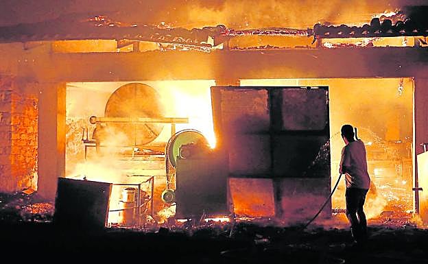 Un hombre echa agua con una manguera al interior de una fábrica de aceitunas devorada por las llamas en la aldea griega de Rovies.