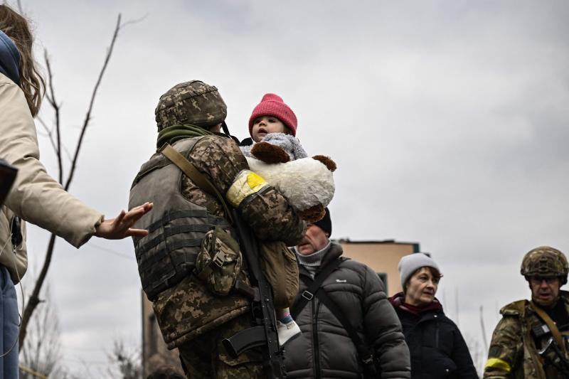 Un militar ucraniano lleva a un niño mientras ayuda a las personas a cruzar un puente destruido en la ciudad de Irpin.