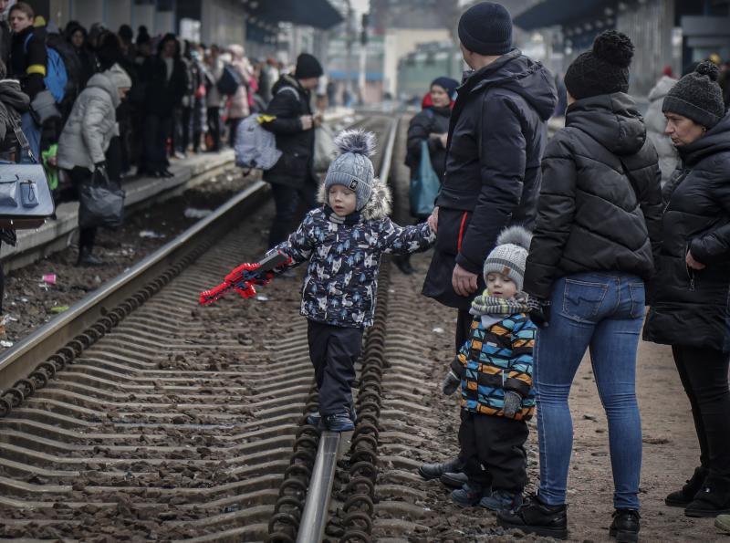 Unos niños ucranianos y sus familiares esperan sobre la vía del tren la llegada del tren en la estación de Kiev.