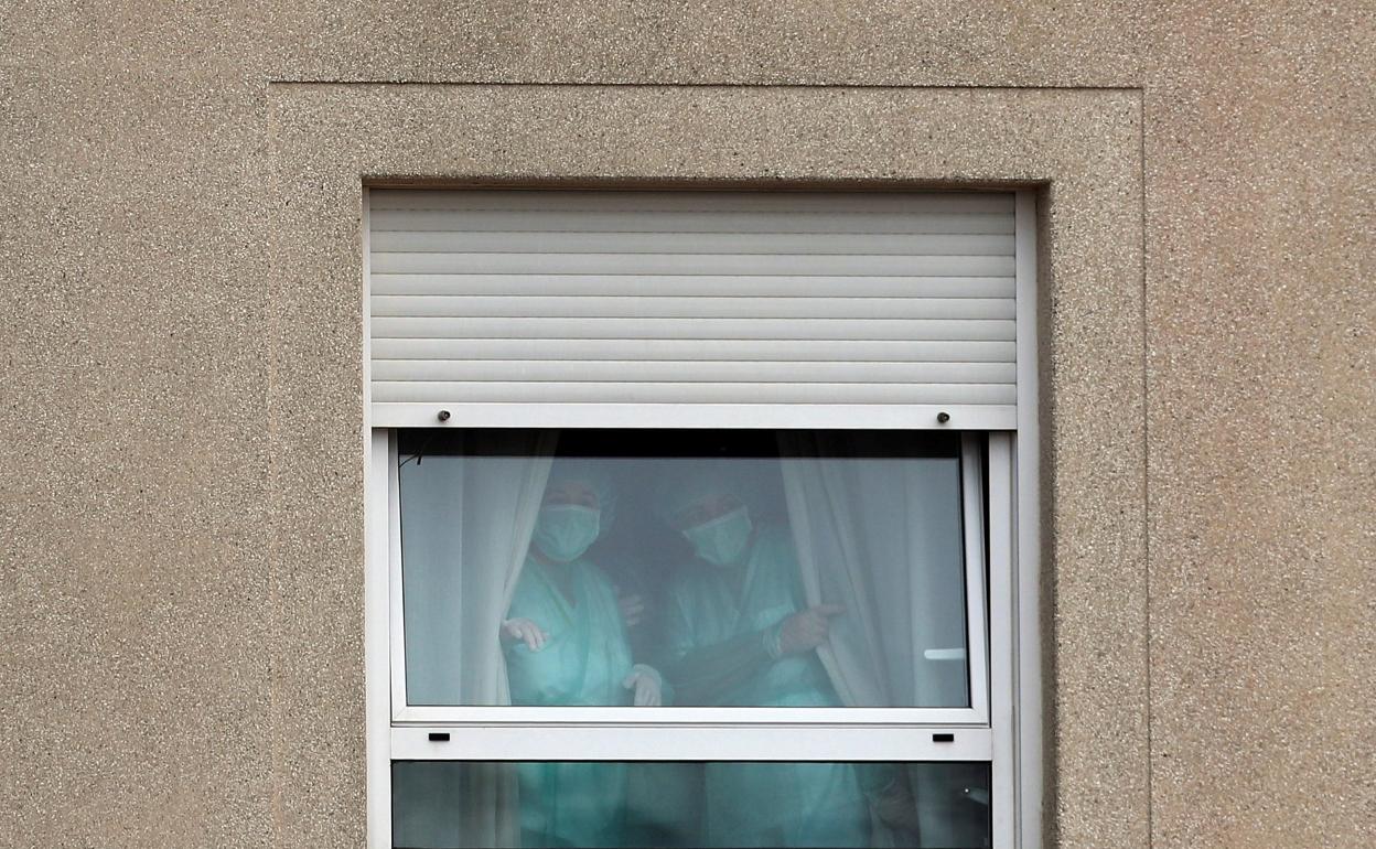 Tras la ventana, profesionales sanitarios. 