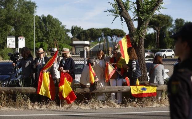 Imagen principal - Un grupo de personas espera la llegada del Rey emérito a la Zarzuela con banderas de España.