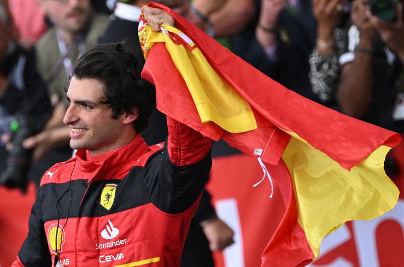 Carlos Sainz alza la bandera española que sujeta en su mano izquierda.