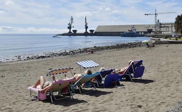 Un grupo de turistas toma el sol junto al puerto industrial de El Pajar. 