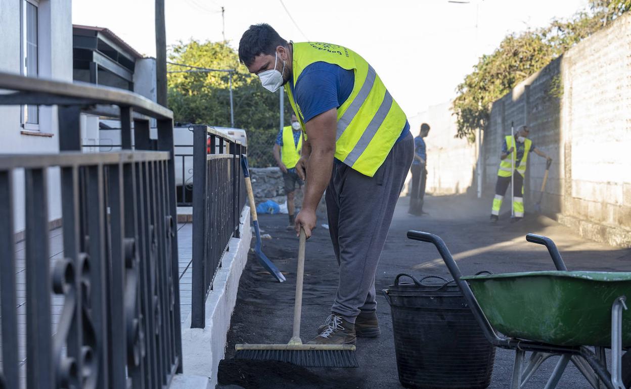 Varias personas retiran cenizas del volcán en las inmediaciones de una casa. 