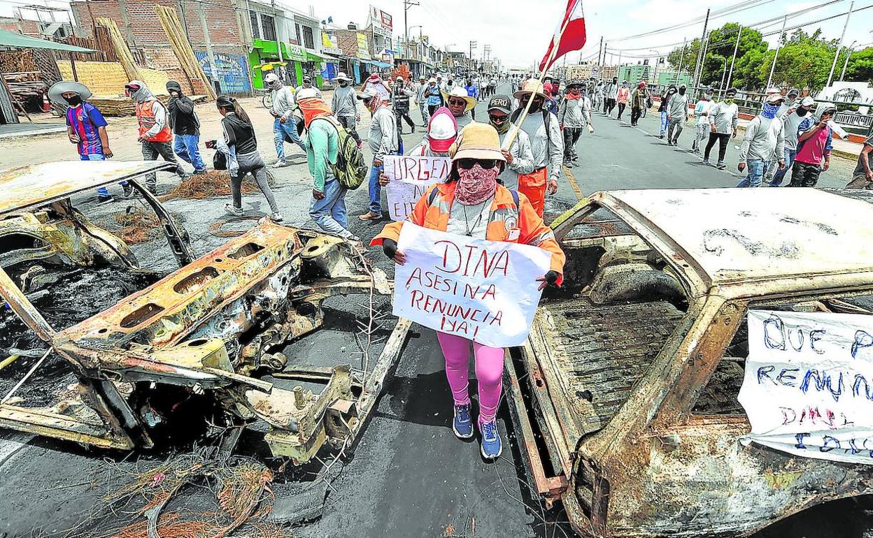 Simpatizantes de Castillo caminan entre dos vehículos incinerados en Arequipa mientras se manifiestan para pedir la salida de Din a Boluarte y el cierre del Congreso.