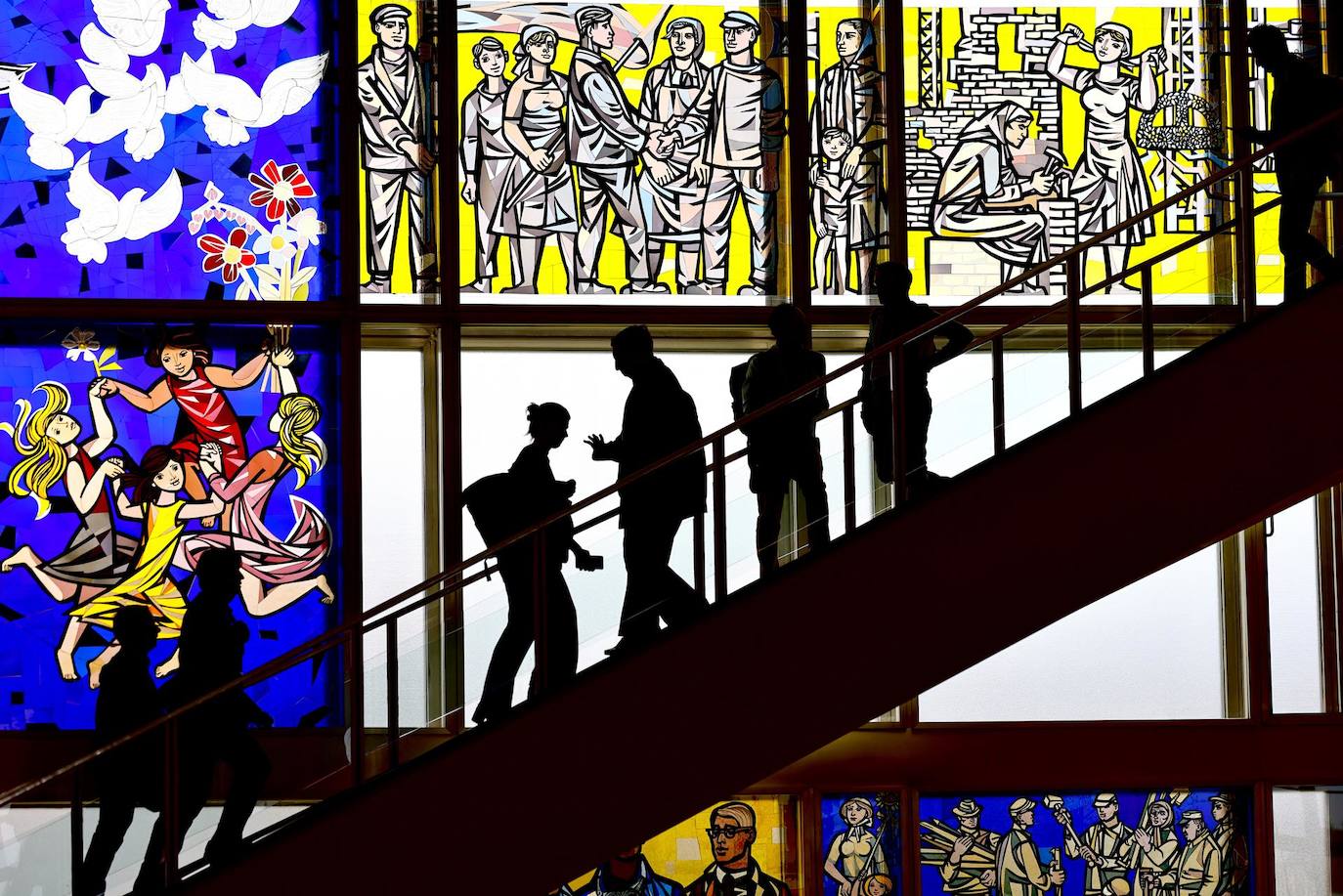 La gente pasa murales de vidrio inspirados en el socialismo en el edificio del Consejo de Estado de la antigua República Democrática Alemana en Berlín, Alemania. La casa fue construida en 1962-64 como el primer edificio representativo de la entonces Alemania Oriental comunista tras la construcción del Muro de Berlín. Después de la caída del Muro de Berlín, el antiguo edificio del Consejo de Estado sirvió como sede del oficial de reubicación del Gobierno Federal desde 1996, como sede provisional del Gobierno Federal de 1999 a 2001, y antes y después como edificio para eventos. , exposiciones y congresos.