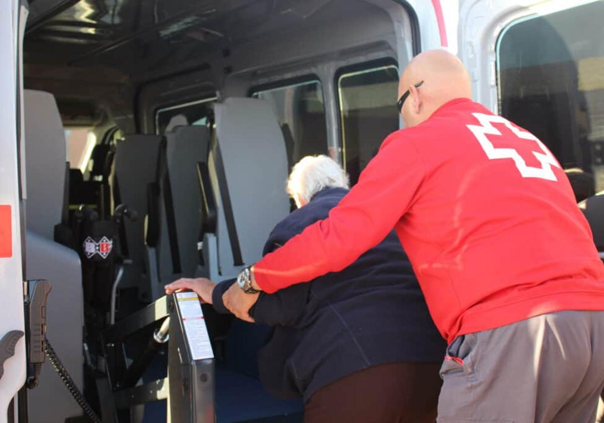 Voluntario de Cruz Roja ayuda a subir a un transporte adaptado a una mujer.