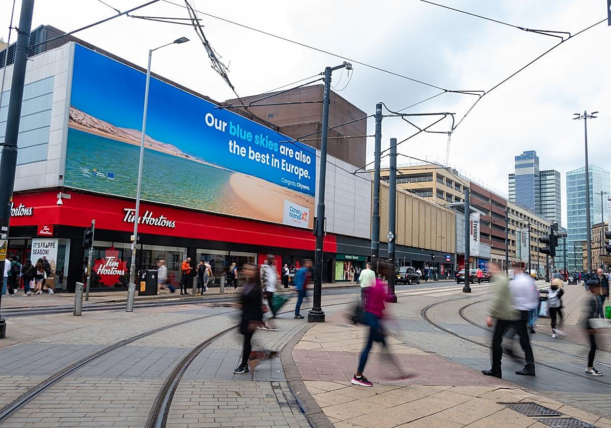 La valla gigante con la foto de la marisma de Jandía y su cielo azul permanecerá catorce días en Market Street, la calle principal de compras de Manchester.