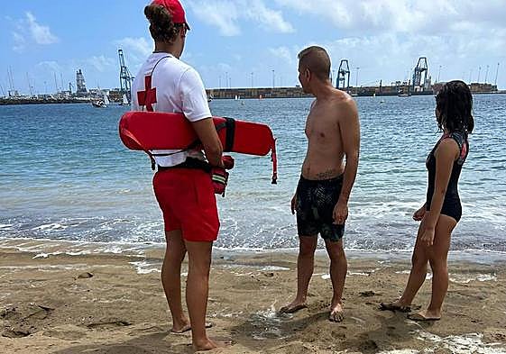 Un socorrista de Cruz Roja informa a dos usuarios de Las Alcaravaneras de la prohibición del baño.