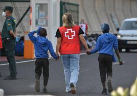 Un efectivo de la Cruz Roja escolta a dos de los menores que viajan, entre a otros 313 inmigrantes que llegaron al puerto de La Estaca en El Hierro.