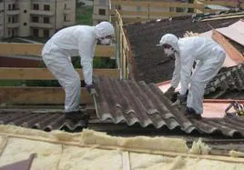 Dos trabajadores en tareas de retirada de planchas de uralita de la cubierta de un edificio.