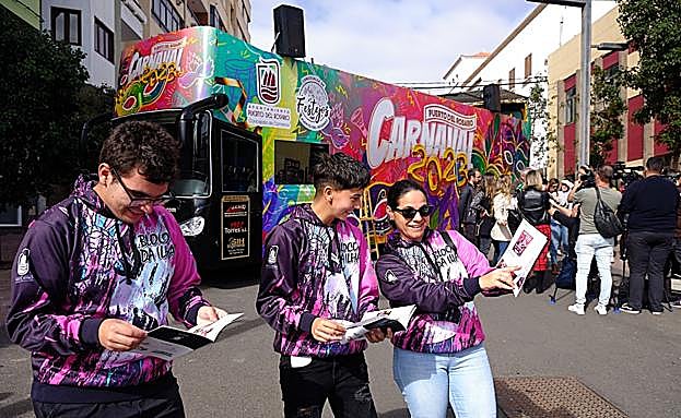 Carnavaleros con el programa de actos en la mano y la guagua al fondo. 