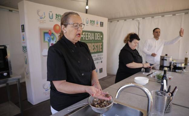 Felisa enseña un caracol a los asistentes a 'Cocinando el Sureste', mientras Sari López prepara el majado de la receta. Al fondo, Yeray Sosa, que ejerce de presentador, dialoga con el público. 
