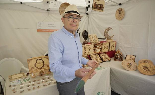 Segundo Cabrera agarra uno de los palos de senderismo que este artesano personaliza con la técnica del pirograbado. 