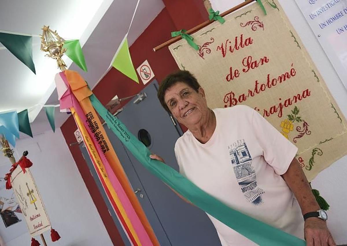 Imagen secundaria 1 - En la foto superior, espectacular mural junto al que pasará la romería. Debajo, una vecina posa con la Vara de la Romera, y una de las cruces engalanadas que estos días luce El Tablero.