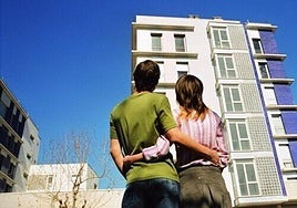 Una pareja contempla un edificio de viviendas.
