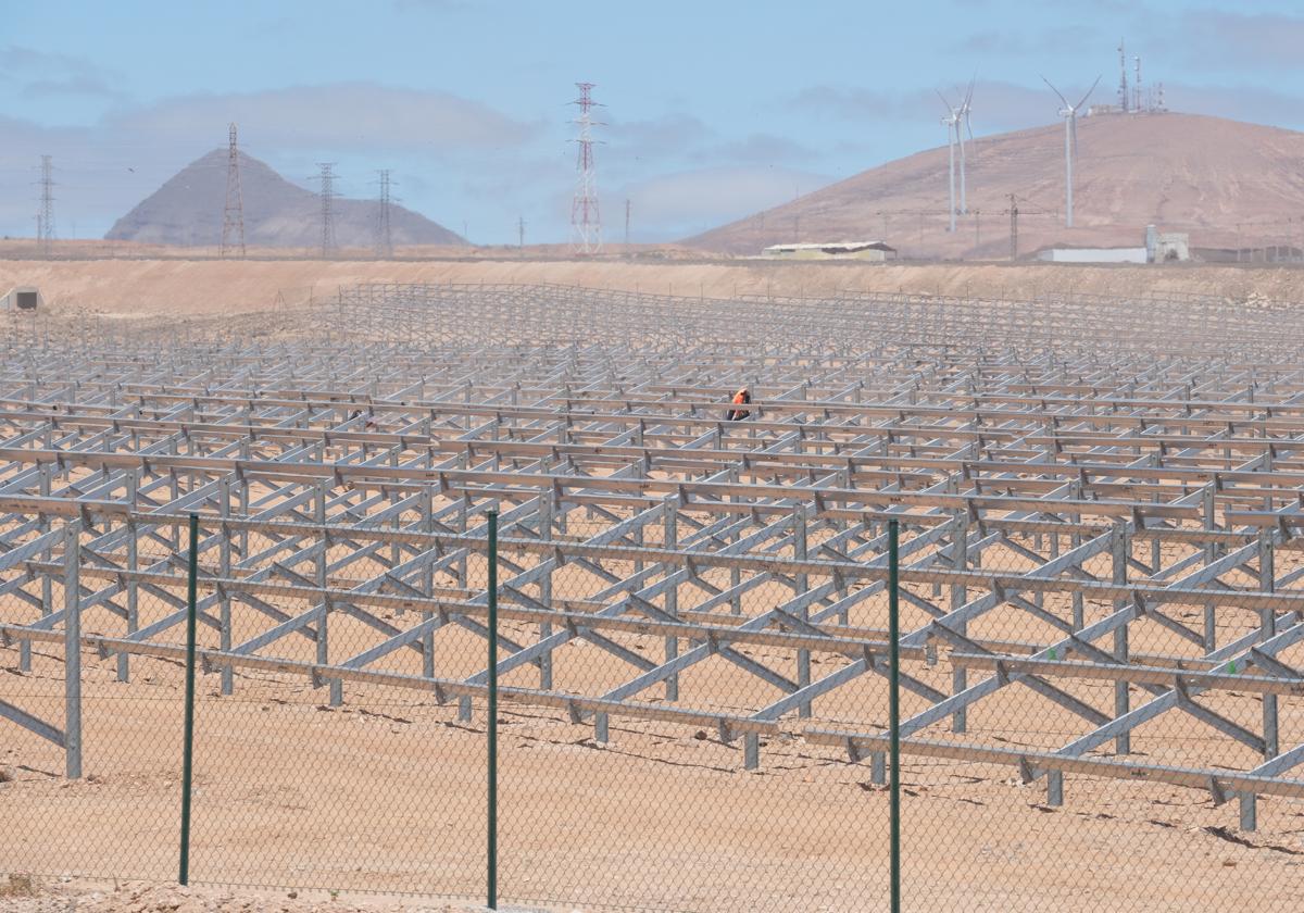 Trabajador instalando placas solares en el parque cercano a la autovía de Puerto del Rosario, con torretas de alta tensión y aerogeneradores al fondo.