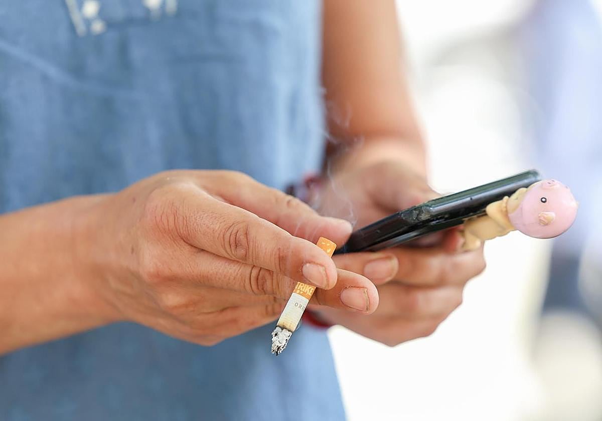 Un fumador hace uso del móvil con el cigarrillo encendido.